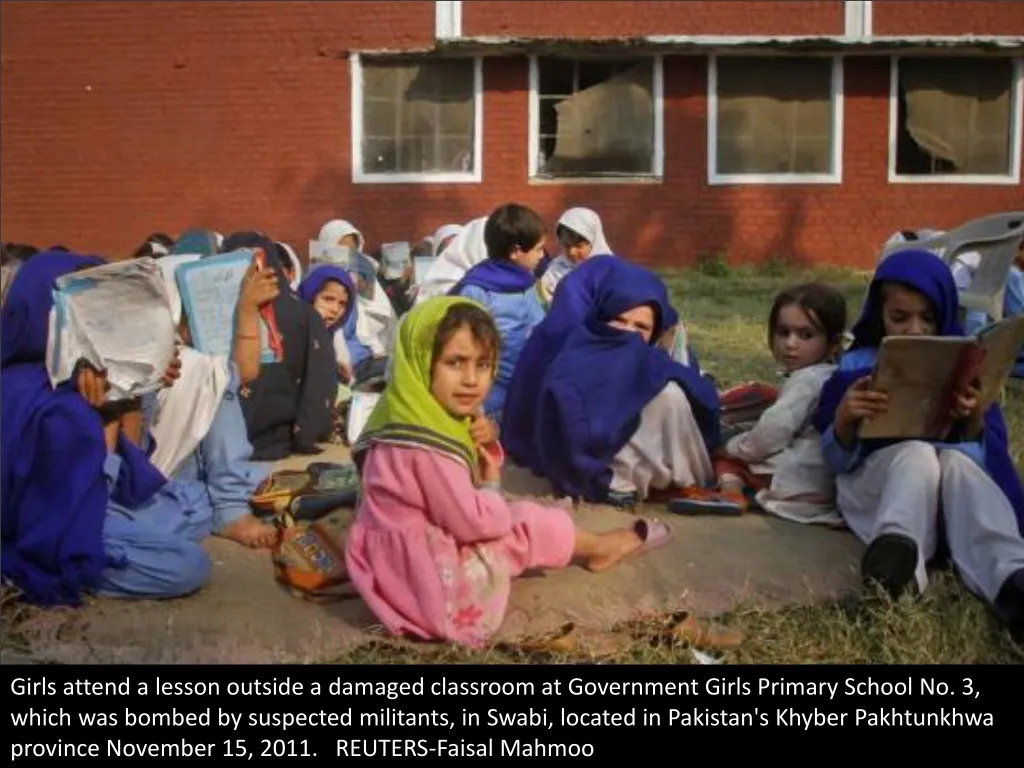 girls attend a lesson outside a damaged classroom